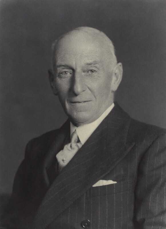 A black and white photograph of the bust and head of Henry Badeley. He has thinning white hair and is wearing a suit and tie. The jacket is pinstriped and has a pocket square. 